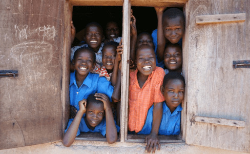 African children smiling happily in front of a school wall